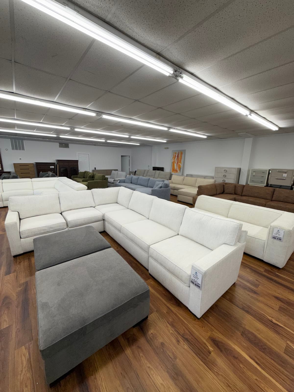 White sectional sofas and a gray ottoman lined up on the sale floor