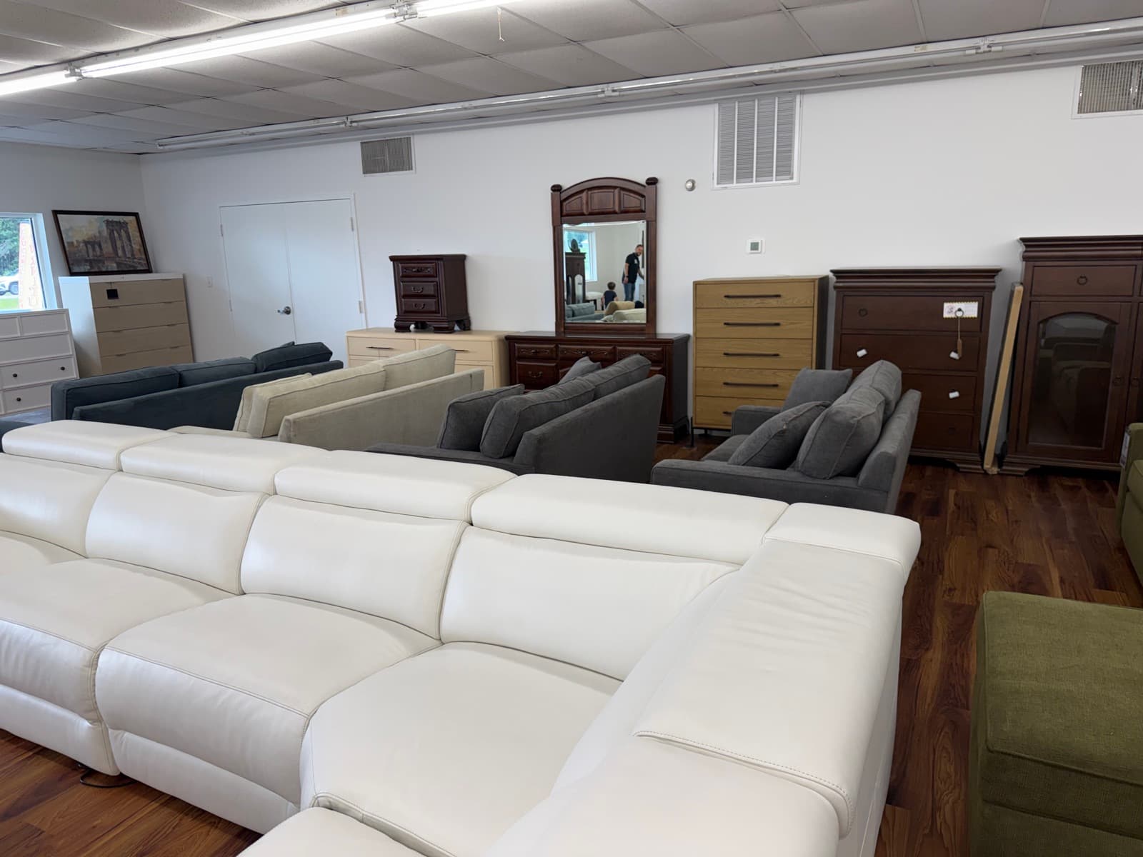 White leather sectional with gray sofas and bedroom dressers behind it