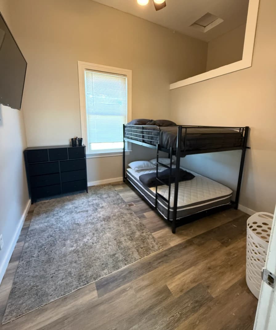 A furnished shared room at Rebuilding Life Sober Living Home with bunk beds made, a dresser, and a TV
