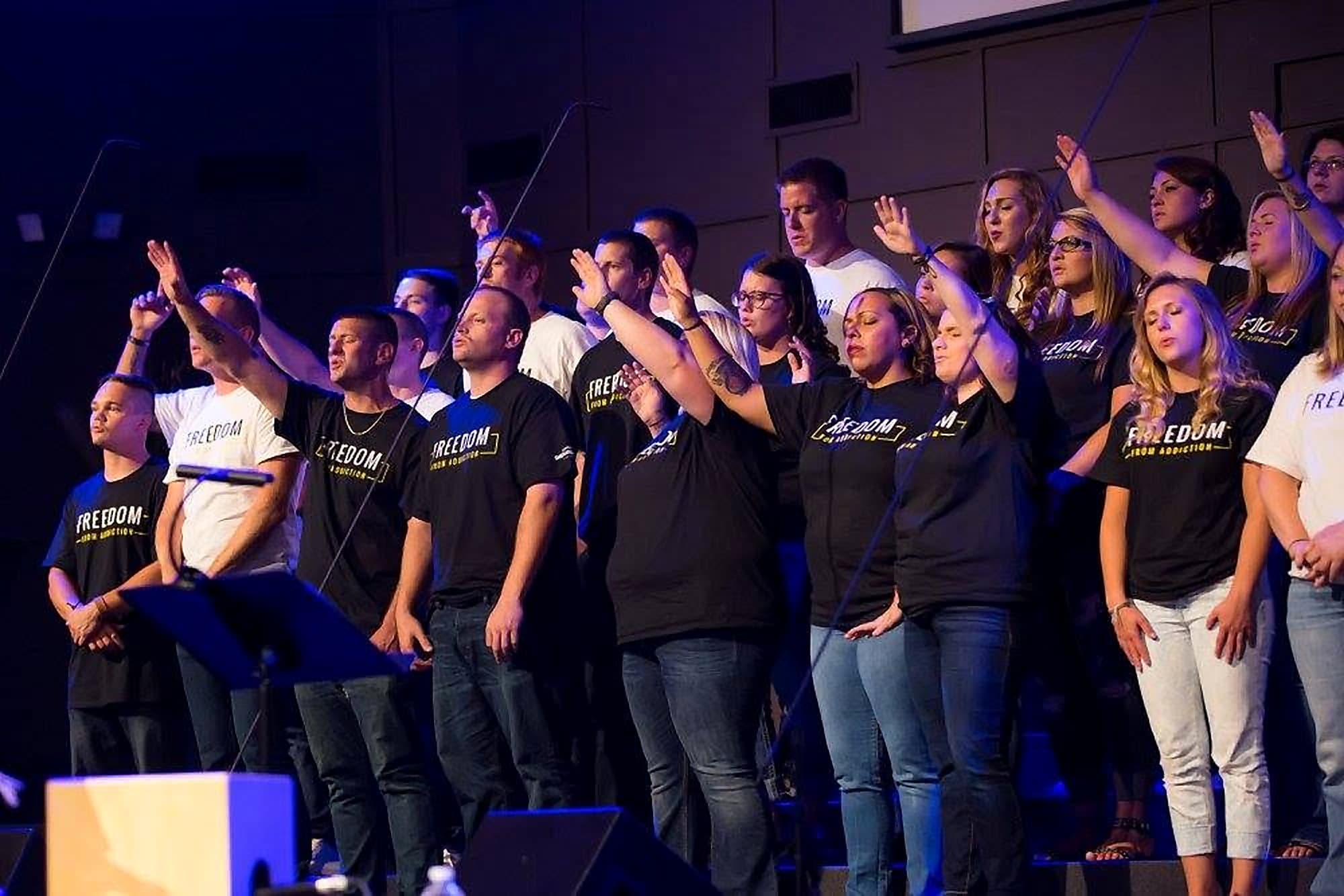 A choir in Freedom From Addiction shirts singing with hands raised at a Shenandoah Valley Teen Challenge event