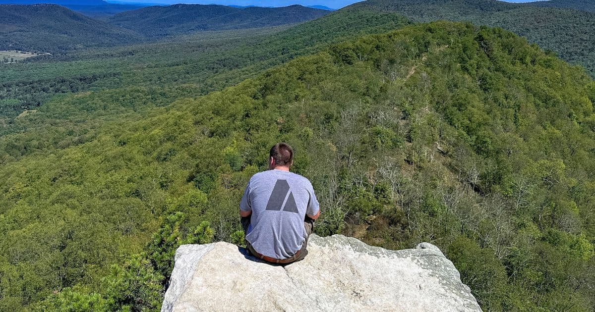 A man sitting on a rock ledge overlooking the Shenandoah Valley mountains