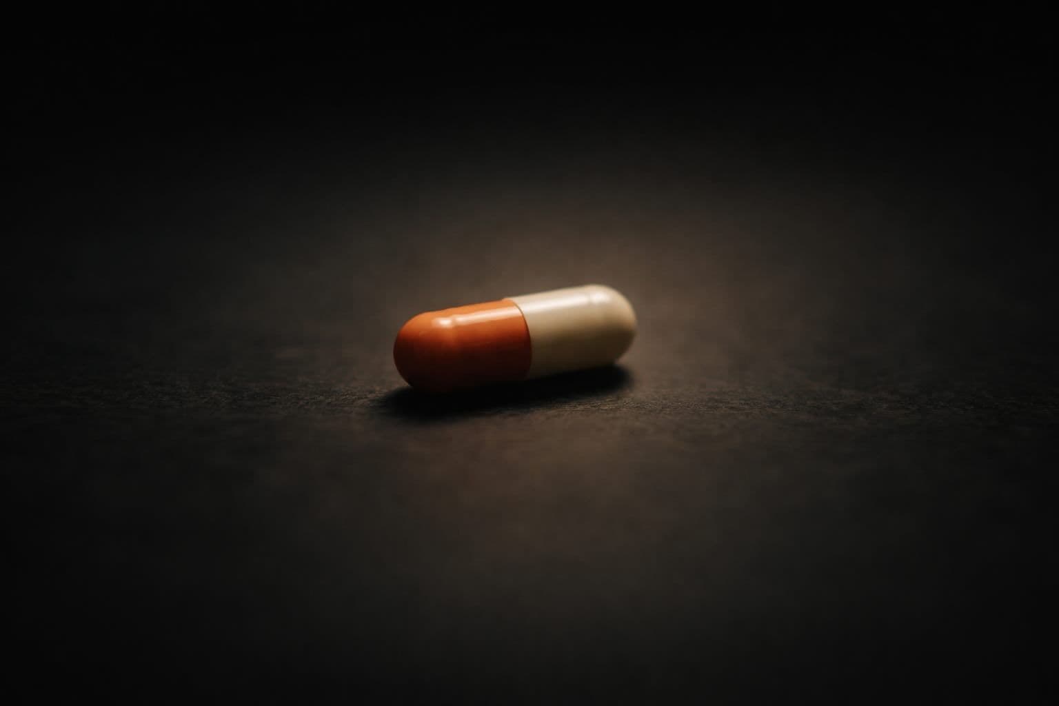 A single pill on a dark surface under dim overhead light, representing the hidden danger of cychlorphine contamination in street drugs.