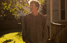 A young man stands on a porch at golden hour in a quiet Virginia backyard, looking ahead with quiet hope and reflection after recovery