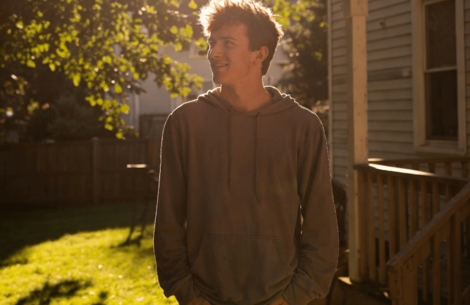 A young man stands on a porch at golden hour in a quiet Virginia backyard, looking ahead with quiet hope and reflection after recovery