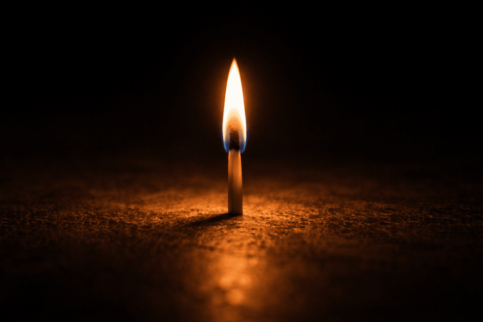 Single lit match flame in darkness, warm orange light on rough surface, representing a small light holding back the dark