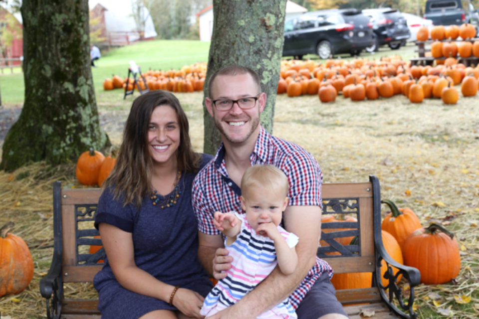 A young couple sits on a bench at a pumpkin patch, smiling with their toddler daughter—once both trapped in addiction, now living in freedom and serving in ministry together.